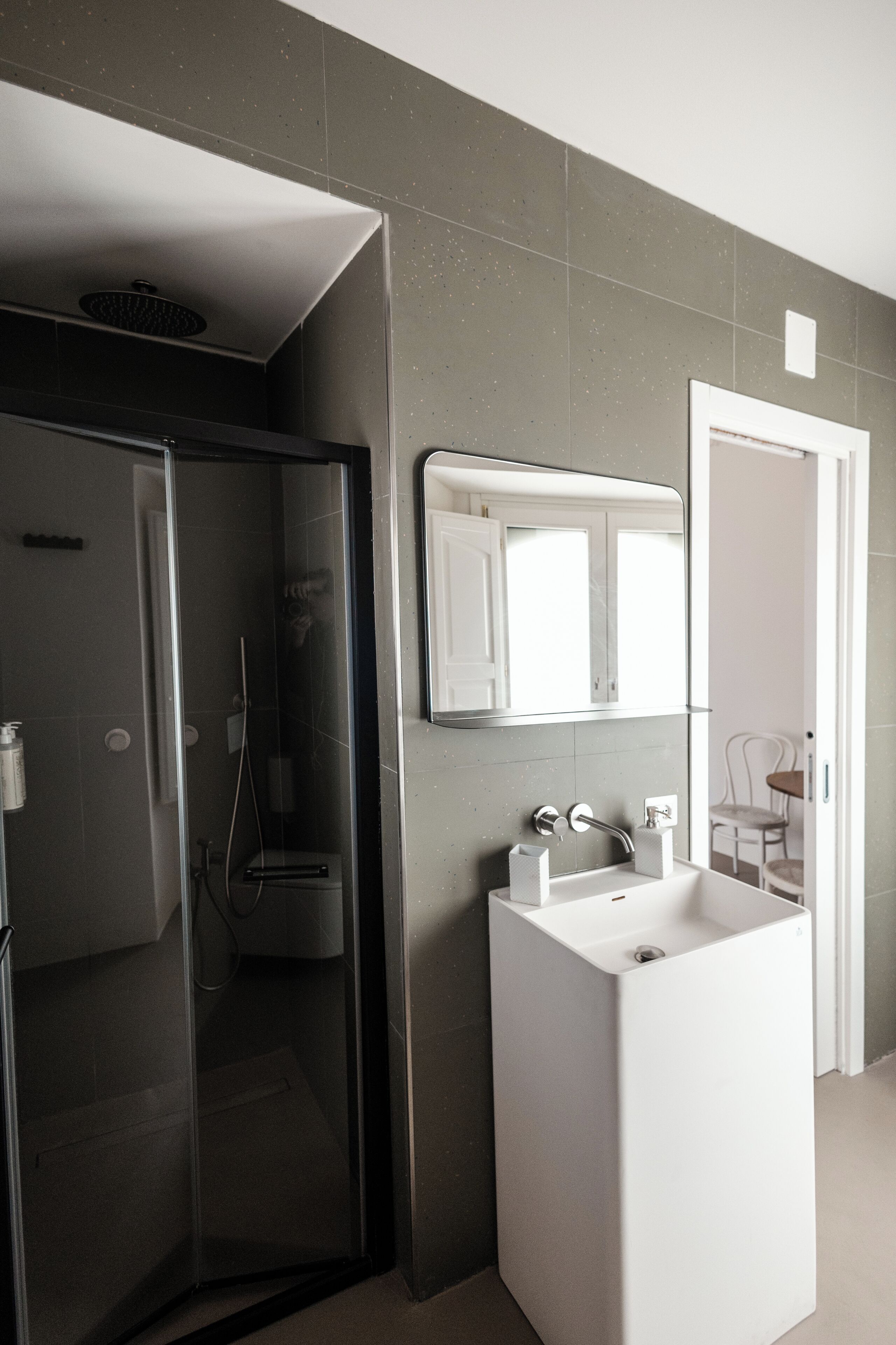 Ein modernes Badezimmer mit einer gläsernen Dusche, einem weißen Waschbecken und einem Spiegel darüber.