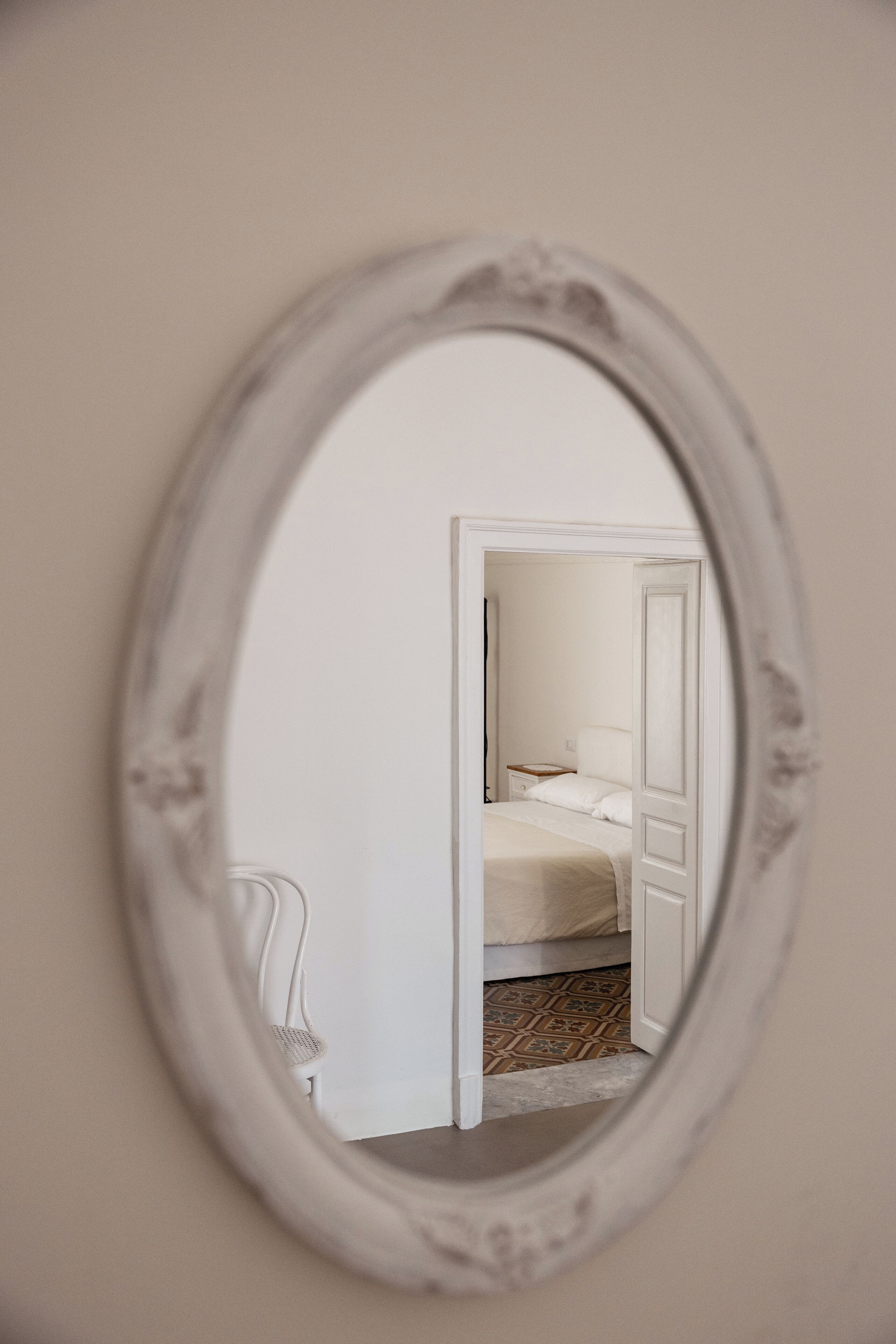 Un espejo refleja un dormitorio con una cama, una mesita de noche y una silla.
