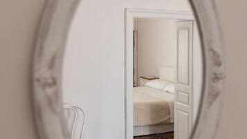 Un espejo refleja un dormitorio con una cama, una mesita de noche y una silla.