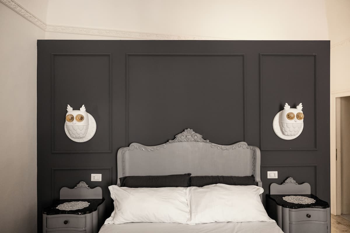 Un dormitorio con un cabecero de paneles oscuros, dos mesitas de noche con arte mural decorativo de búhos y una cama con ropa de cama blanca.
