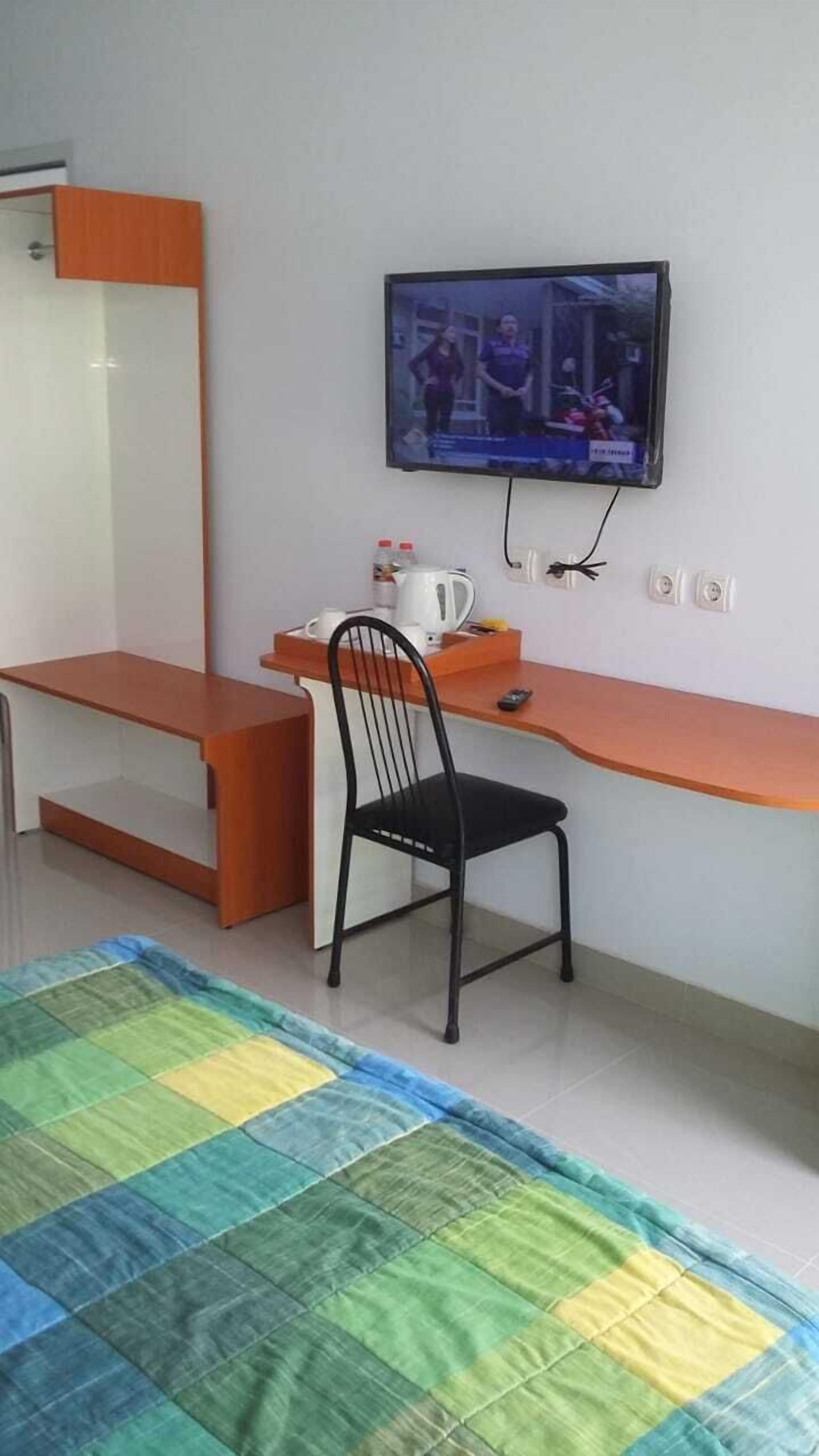A small room with a desk, chair, television, and a colorful rug.