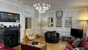 Uma sala de estar com lareira, um sofá de couro preto, um sofá vermelho, uma mesa de centro de vidro e uma poltrona de couro preto.