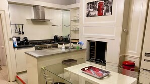 Cozinha moderna com ilha central, eletrodomésticos de aço inoxidável e área de jantar com mesas e cadeiras de vidro.