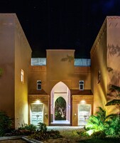 Un edificio con una entrada central en arco, dos alas laterales y un cielo nocturno estrellado.