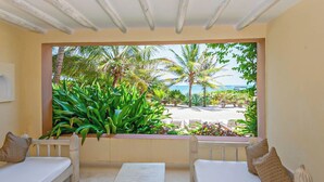 A room with a view of a beach and palm trees, featuring a white sofa and a small table. - Medina Palms (Watamu)