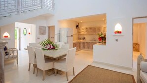 A spacious living area with a dining table, white chairs, and a kitchen in the background. - Medina Palms (Watamu)