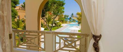 A balcony with a view of a swimming pool, palm trees, and buildings.