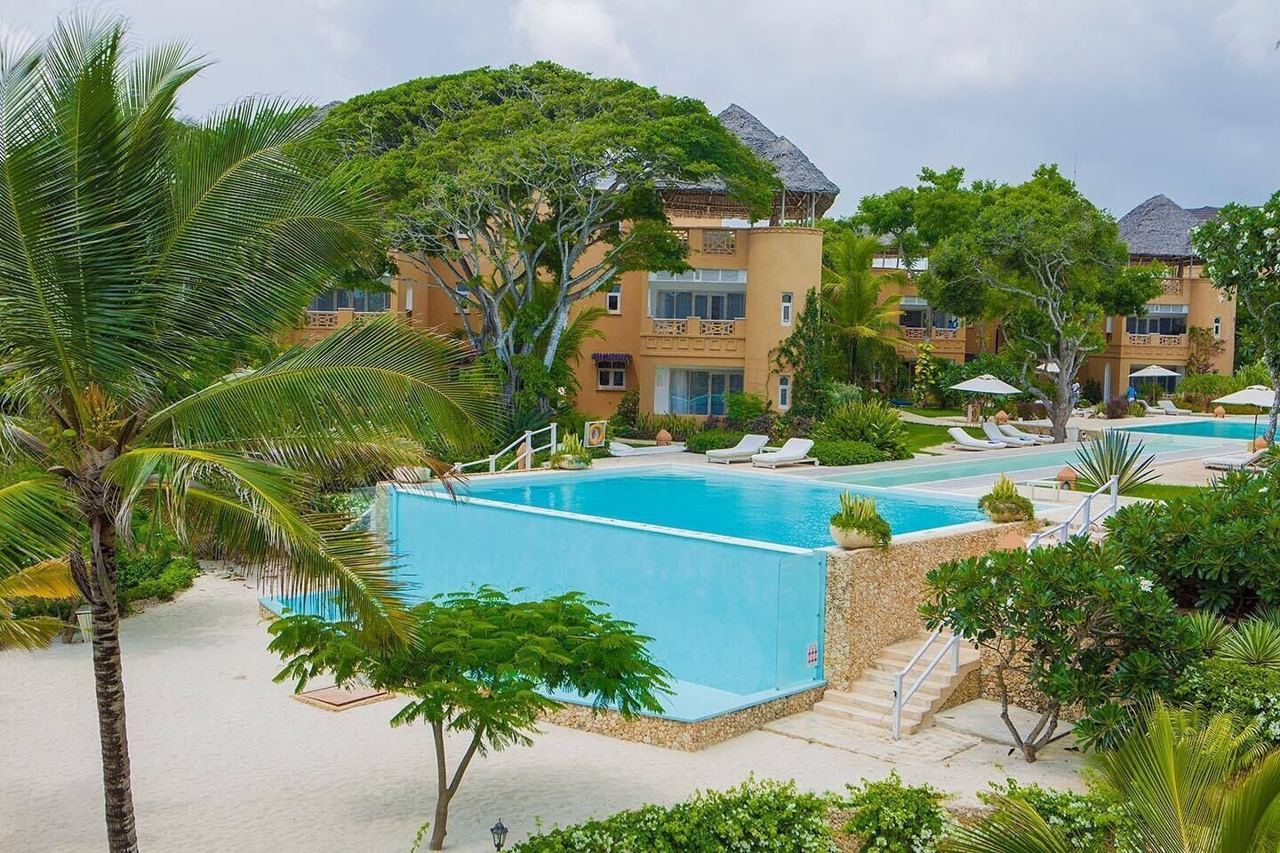 Un resort con zona de piscina, palmeras y un edificio con techo de paja.