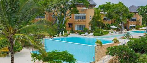 Un resort con zona de piscina, palmeras y un edificio con techo de paja.