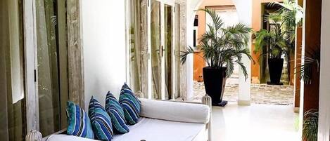 A spacious room with a white sofa, striped pillows, a small wooden table, and a large potted plant.