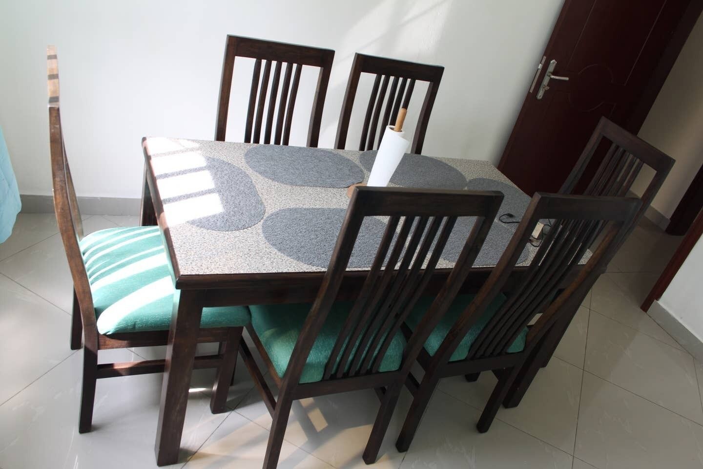 Una mesa de comedor con cuatro sillas, cada una con un cojín verde. La mesa tiene un tablero con diseño gris.