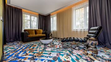 A living room with a patterned carpet, a sofa, a chair, and a large window with curtains.