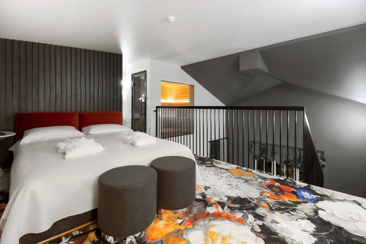 Een moderne hotelkamer met een groot bed, een rood hoofdeinde, een balkon met een zwarte reling en uitzicht op de stad.