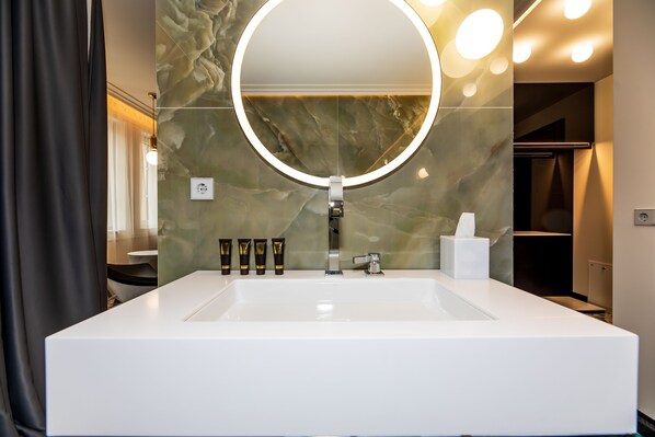 A modern bathroom with a large sink, a round mirror with a light, and toiletries on the counter.