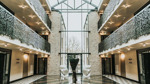A spacious lobby with a checkered floor, a central sculpture, and a glass ceiling. - Amsterdam Plaza (Palanga)