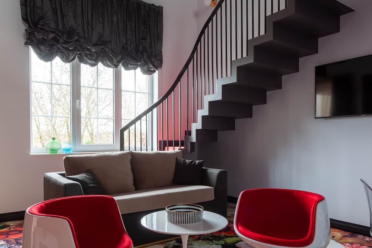 Een moderne woonkamer met een trap, een bank, twee rode stoelen en een bijzettafeltje.