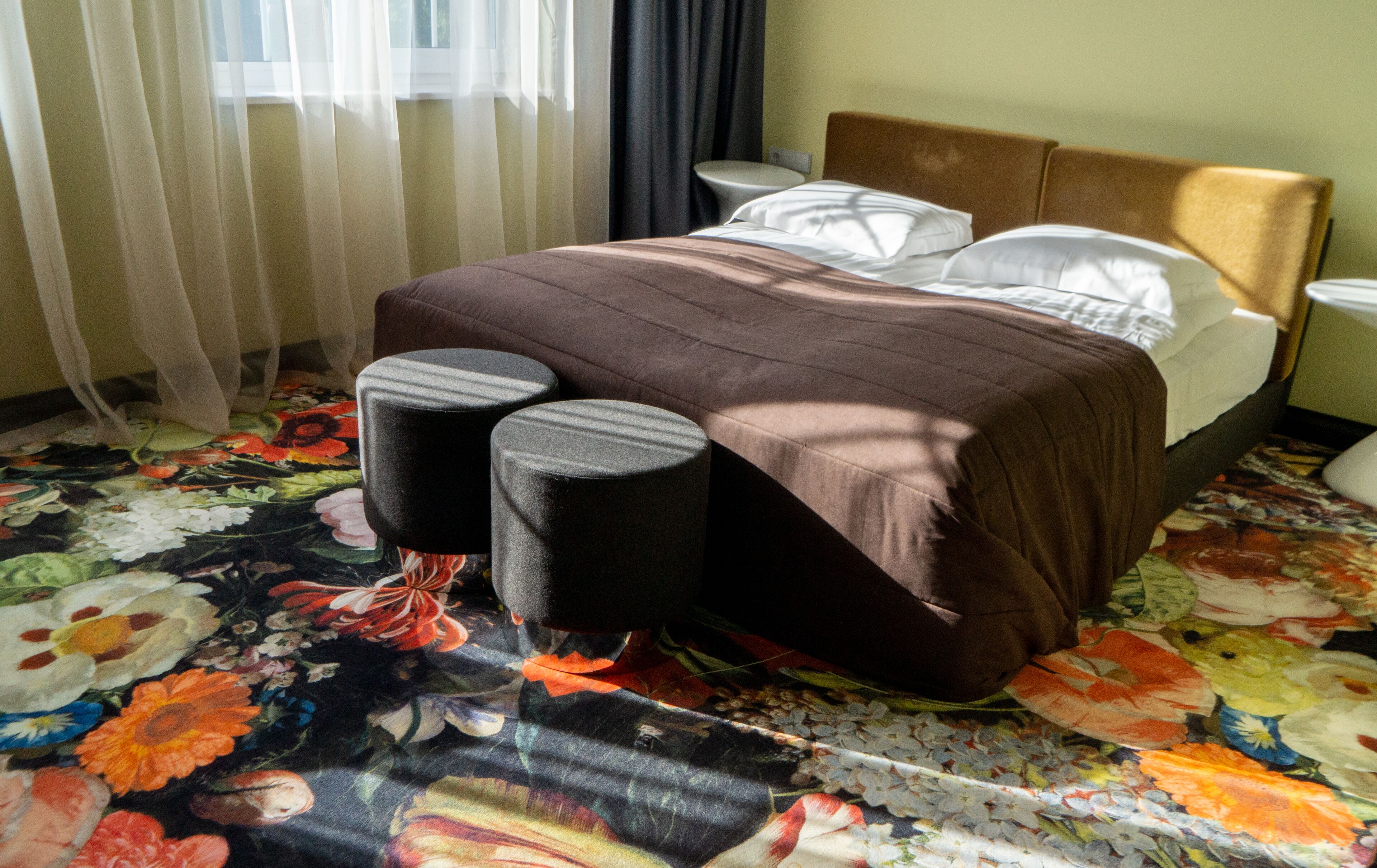 A hotel room with a bed, two bedside tables, a headboard, and a floral carpet.