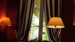 A cozy living room with a sofa, a small table, and two lamps. There is a window with curtains and a view of greenery outside. - La Cordeline (Brignoles)