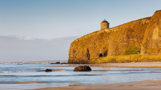 A coastal landscape with a prominent cliff and a small building on top.
