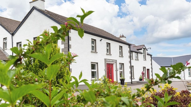 A white building with a red door, surrounded by greenery and flowers. - The Willows House & Studios (Limavady)