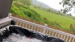 A hot tub with water jets, surrounded by a wooden deck and a view of a green landscape.