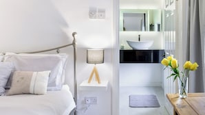 A modern bedroom with a bed, bedside lamp, and a view into a bathroom with a sink and mirror. - The Willows House & Studios (Limavady)