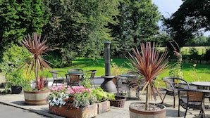 An outdoor patio area with metal chairs and tables, surrounded by potted plants and a large planter with flowers. - The Willows House & Studios (Limavady)