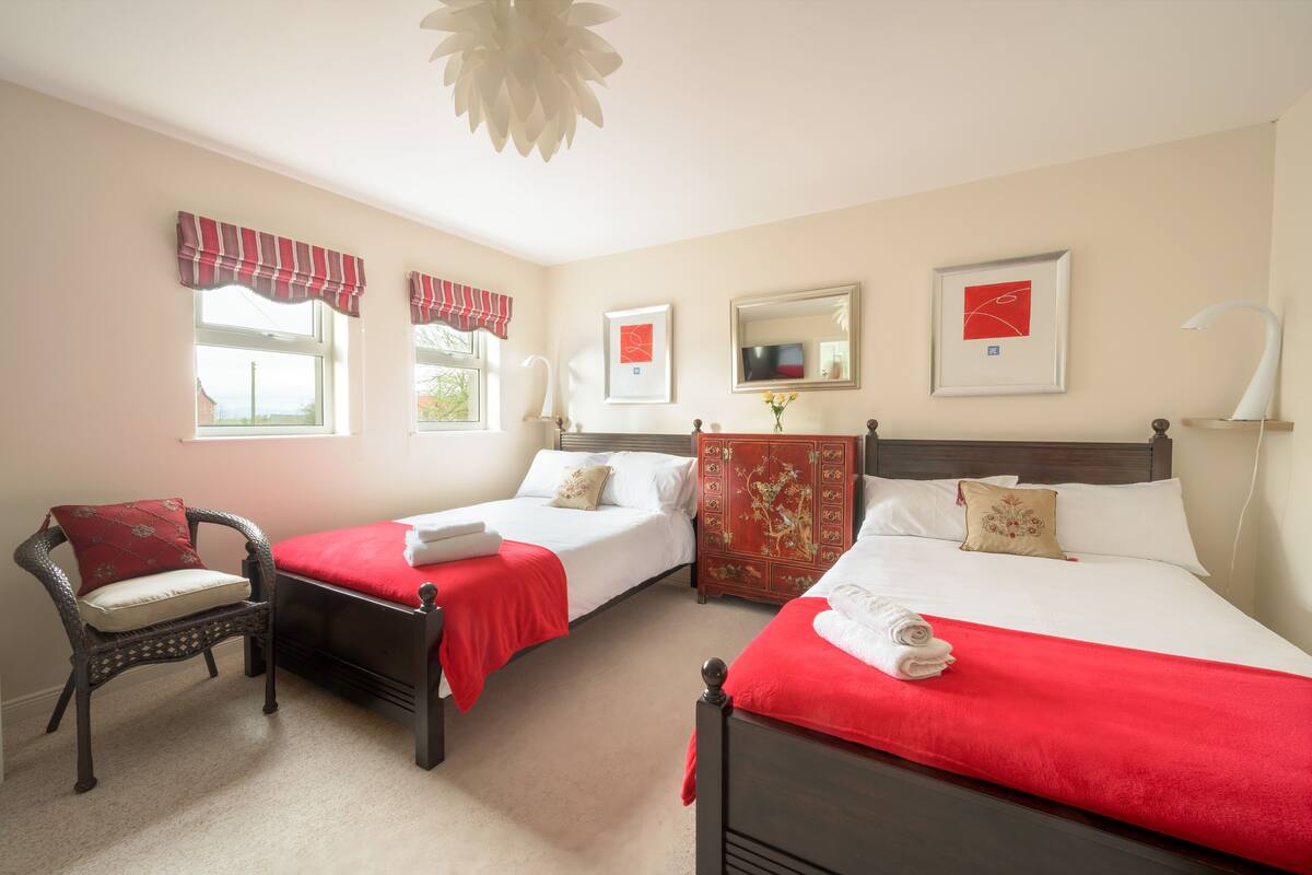 A hotel room with two single beds, a chair, a dresser, and a large mirror.