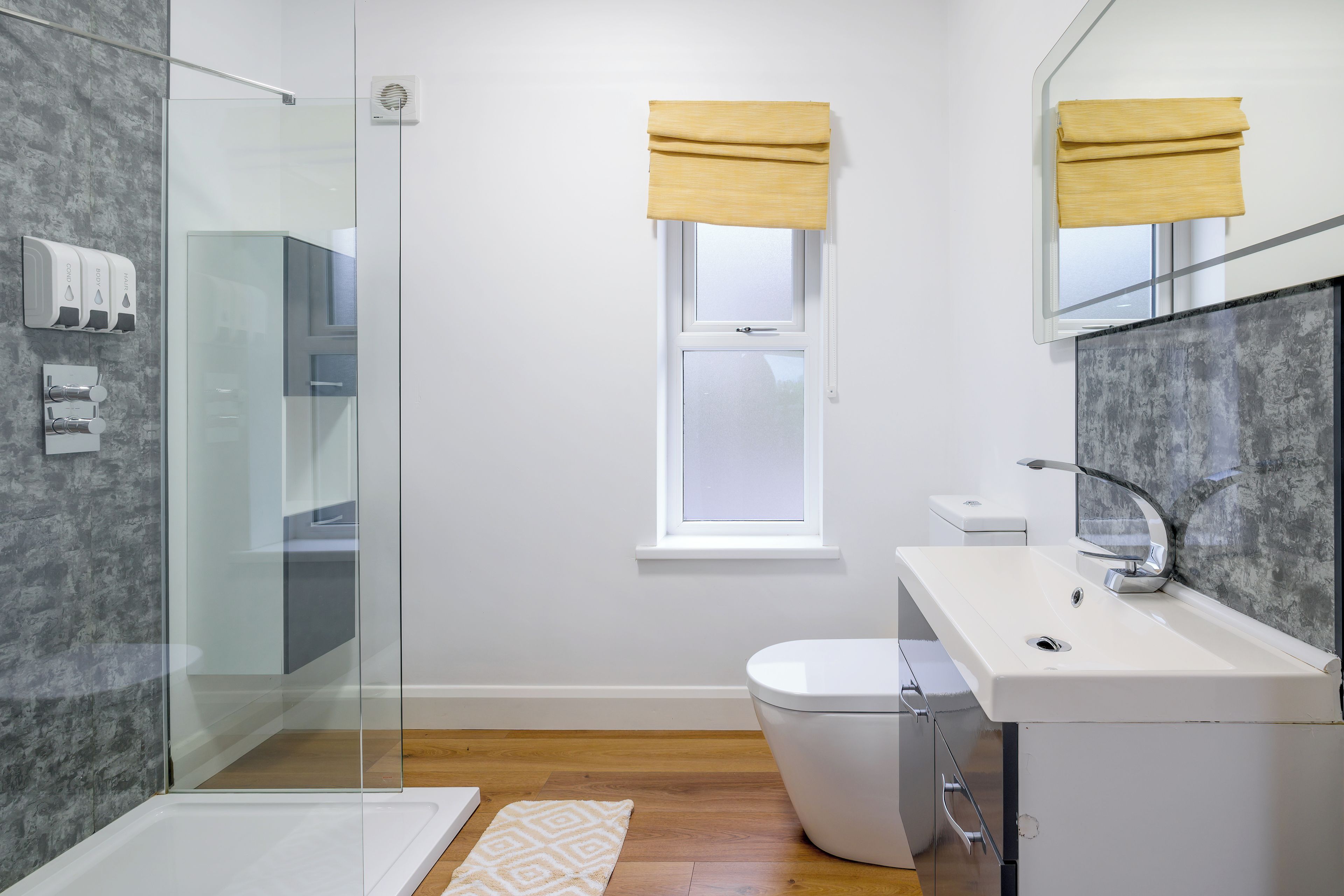 A modern bathroom with a glass shower enclosure, a toilet, and a sink with a mirror.