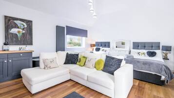A modern bedroom with a sectional sofa, a bed with a grey headboard, and a painting on the wall.
