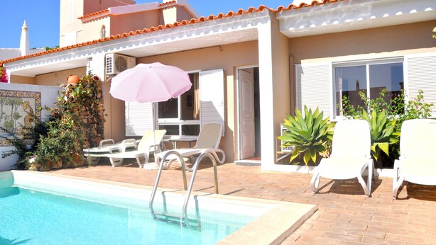 A swimming pool with a pink umbrella, white lounge chairs, and a tiled patio area. - Stylish and well-equipped, private pool, close to amenities, free AC & Wifi (Vilamoura)