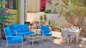Un patio al aire libre con un sofá azul, sillas blancas y una mesa.