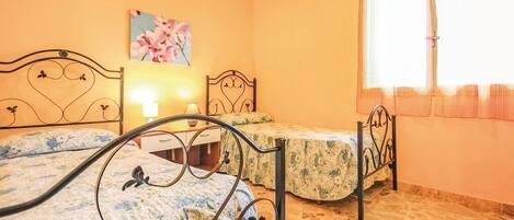 A bedroom with two beds, a nightstand, a lamp, a painting, and a window with curtains.