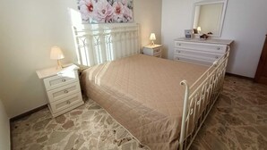 Ein Schlafzimmer mit Bett, Schminktisch, Nachttisch, Spiegel und einem floralen Bild an der Wand.