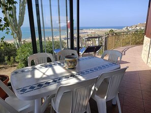An outdoor patio with a table and chairs, a decorative bowl, and a view of the beach and ocean.