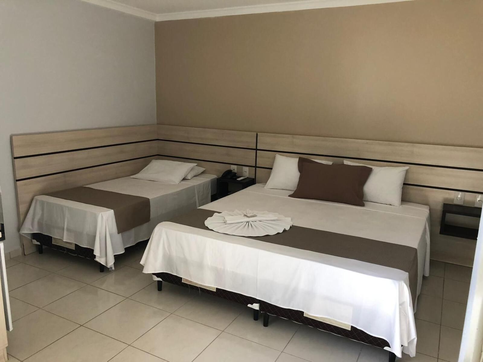 A hotel room with two single beds, a large bed, and a small table with a white cloth.