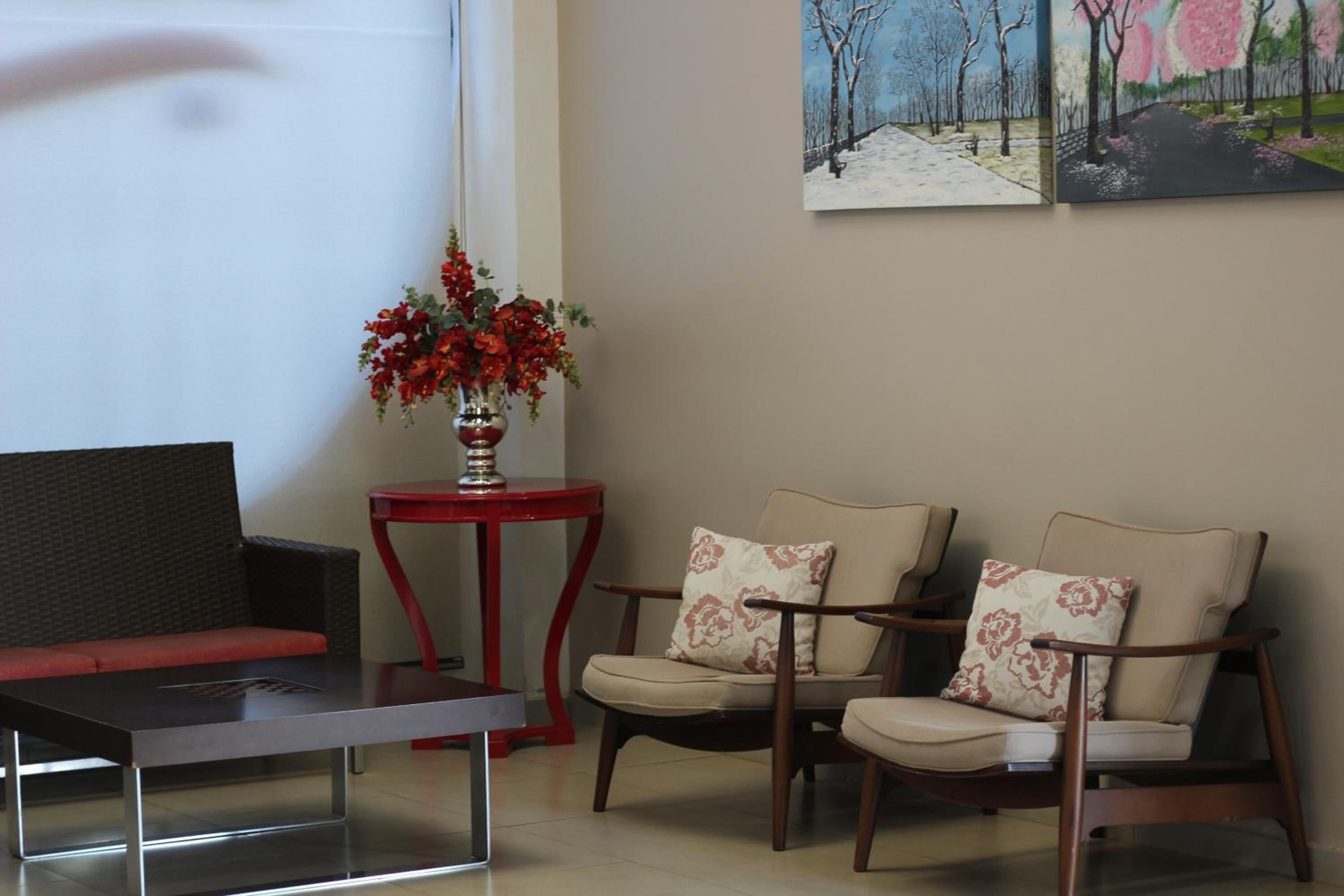 Een moderne woonkamer met een bank, twee fauteuils, een salontafel en een rode bijzettafel met een bloevas.