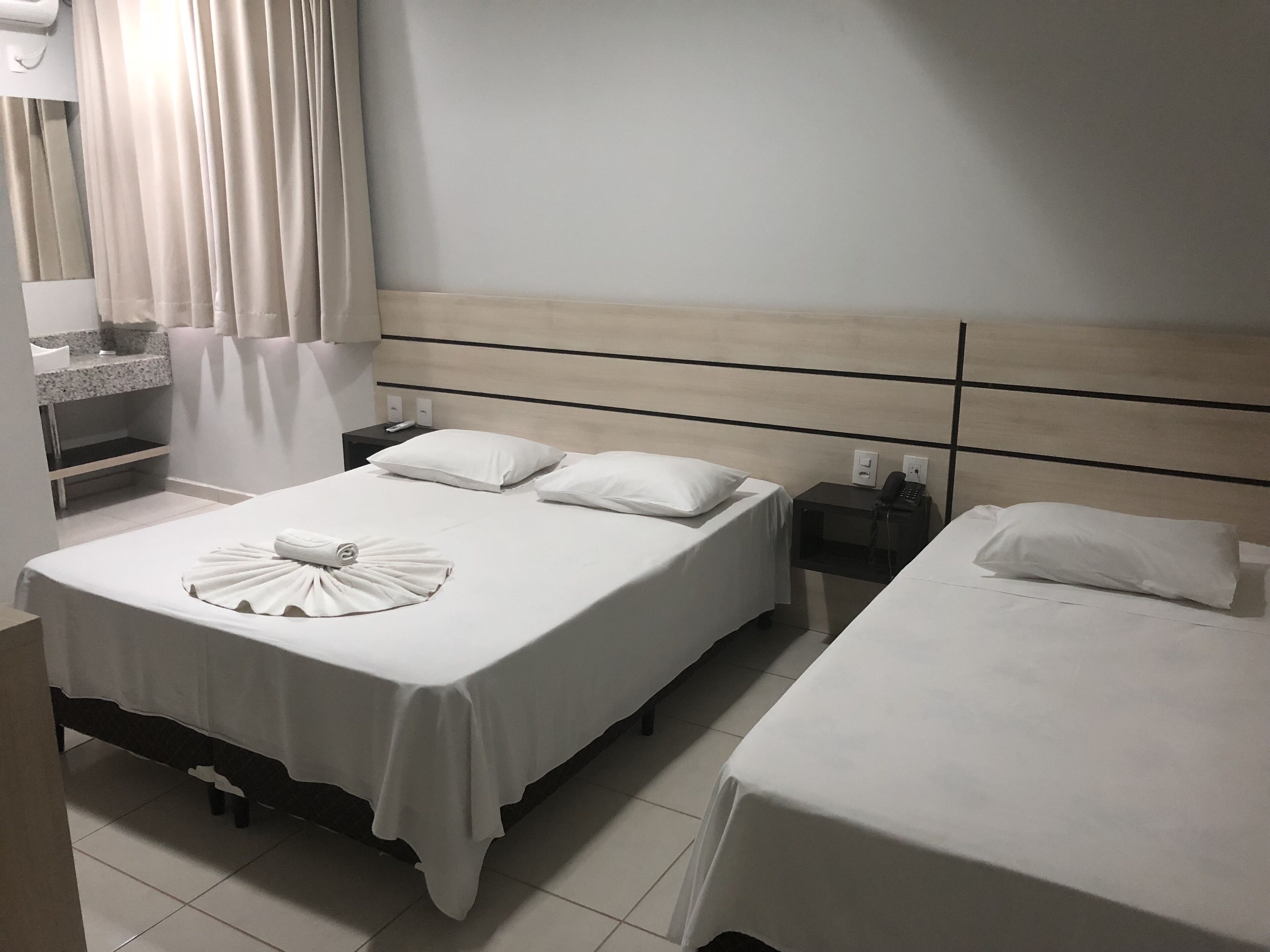 Habitación de hotel con dos camas, una mesita de noche con teléfono y baño con lavabo y espejo.