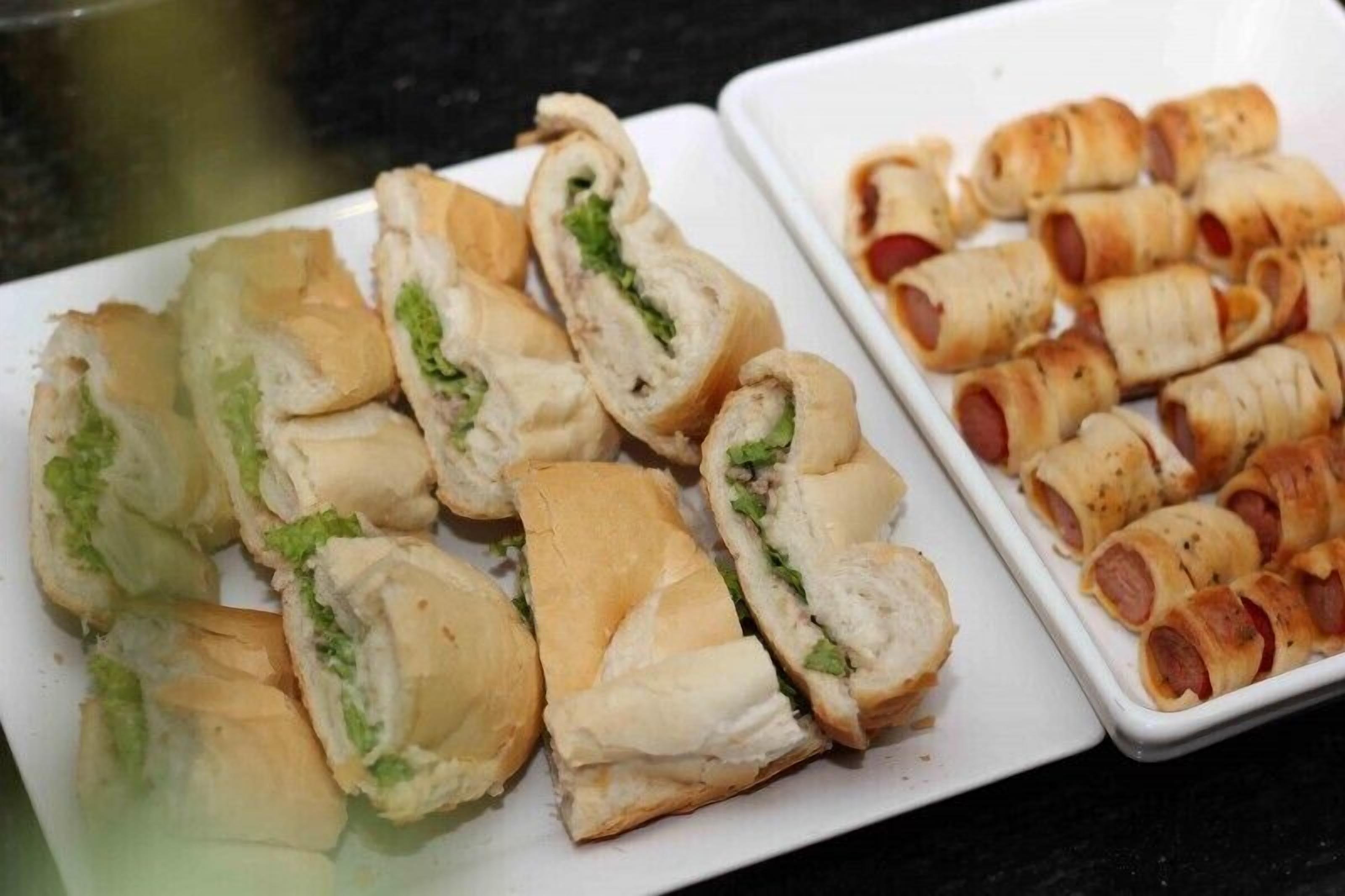 A plate of food with sandwiches and sausage rolls.