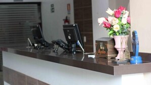 A reception desk with a vase of flowers, a telephone, and a blue object on the counter. - Dallas Hotel (Palotina)