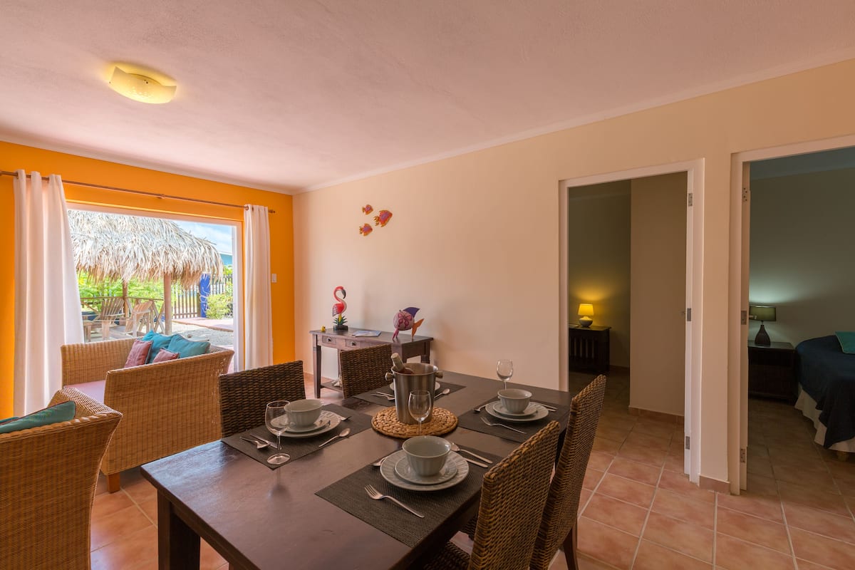 Comedor con una mesa preparada para cuatro, sillas de mimbre y vistas al exterior.
