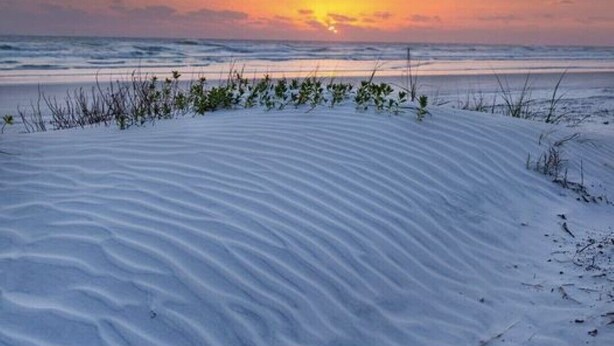 Een strand met duinen en een ondergaande zon.
