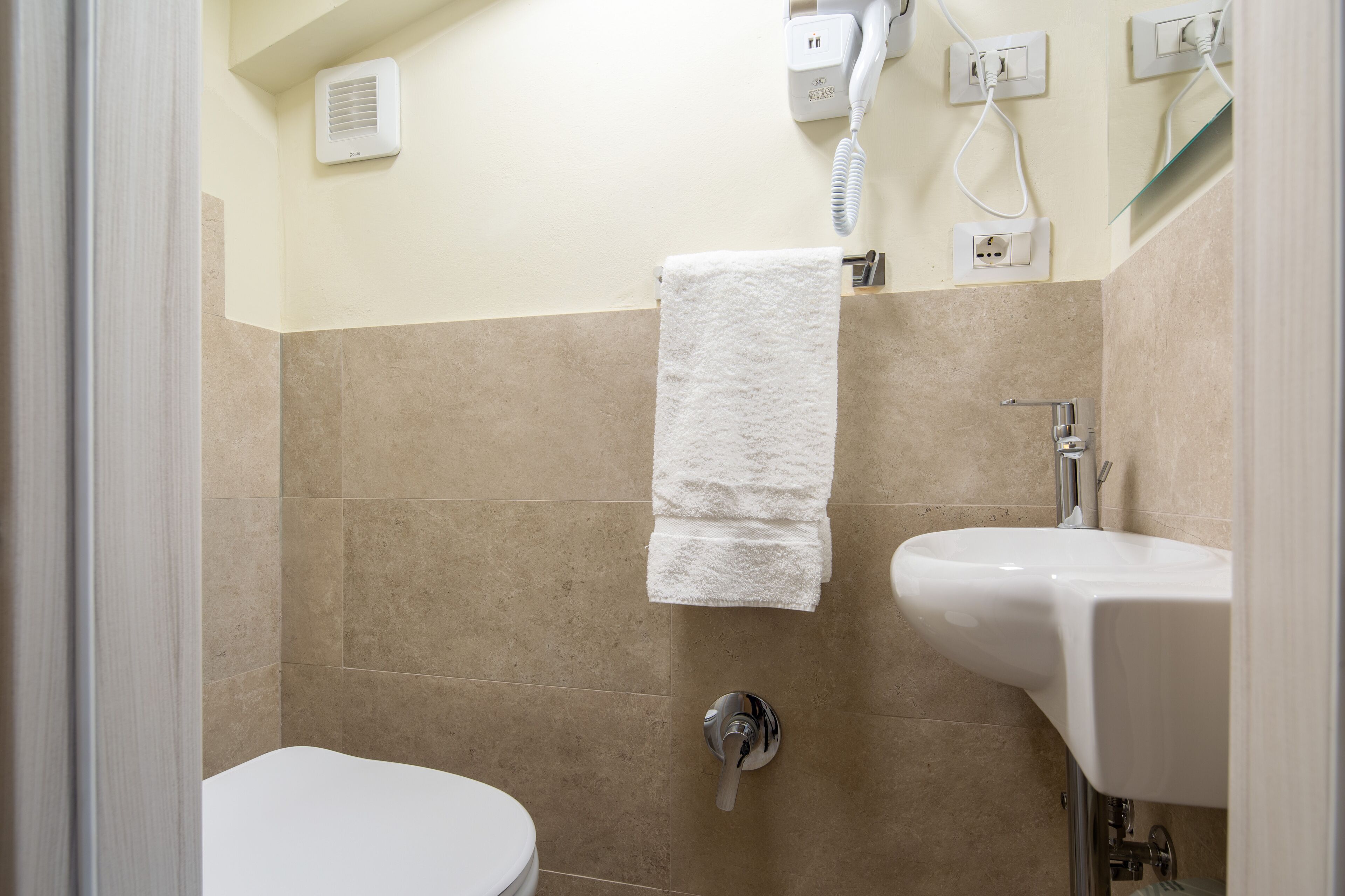 Une salle de bain avec des toilettes, un lavabo, une serviette accrochée au mur et un sèche-cheveux branché.