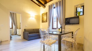 A dining area with a table and chairs, a television on the wall, and a window with curtains. - Duomo Apartments by Mmega (Florence)