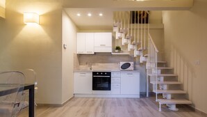 A modern kitchen with white cabinets, a microwave, and a built-in oven. There is a staircase with white railings leading to an upper level. - Duomo Apartments by Mmega (Florence)