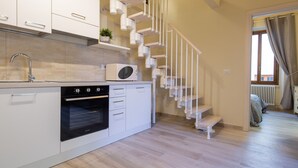A modern kitchen with white cabinets, a built-in oven, and a microwave. A white staircase with a unique design leads to a bedroom area. - Duomo Apartments by Mmega (Florence)