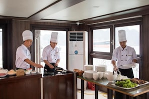 Una cucina professionale con chef che preparano cibo, un grande condizionatore d'aria e un'area buffet con piatti e ciotole.