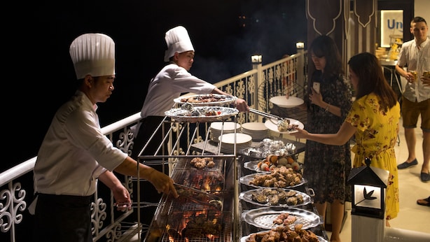 A chef grilling food on a balcony with a railing and a decorative lantern. - Cat Ba White Pearl (Hai Phong)
