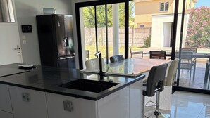 Une cuisine moderne dotée d’un grand îlot central, d’appareils électroménagers en acier inoxydable et donnant sur un espace patio extérieur.