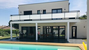 Une maison moderne à deux étages, dotée d’un patio couvert et d’une piscine située à l’avant.